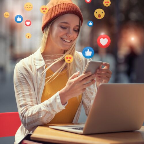 Stock image of a creator using a laptop and phone surrounded by floating social media reaction icons