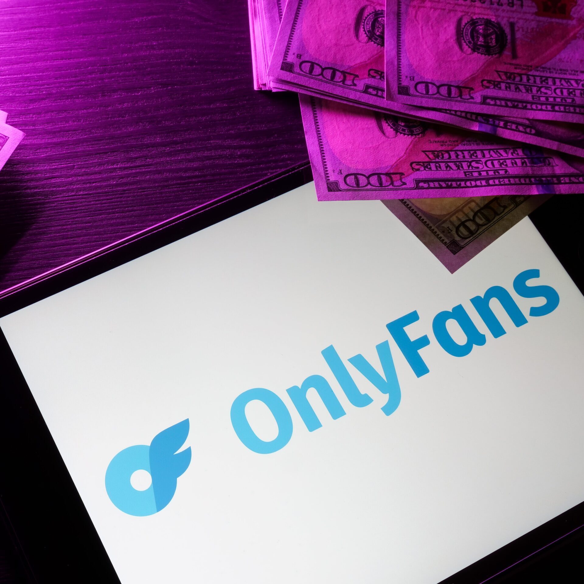 Smartphone screen displaying the OnlyFans logo resting on a desk with purple neon lighting