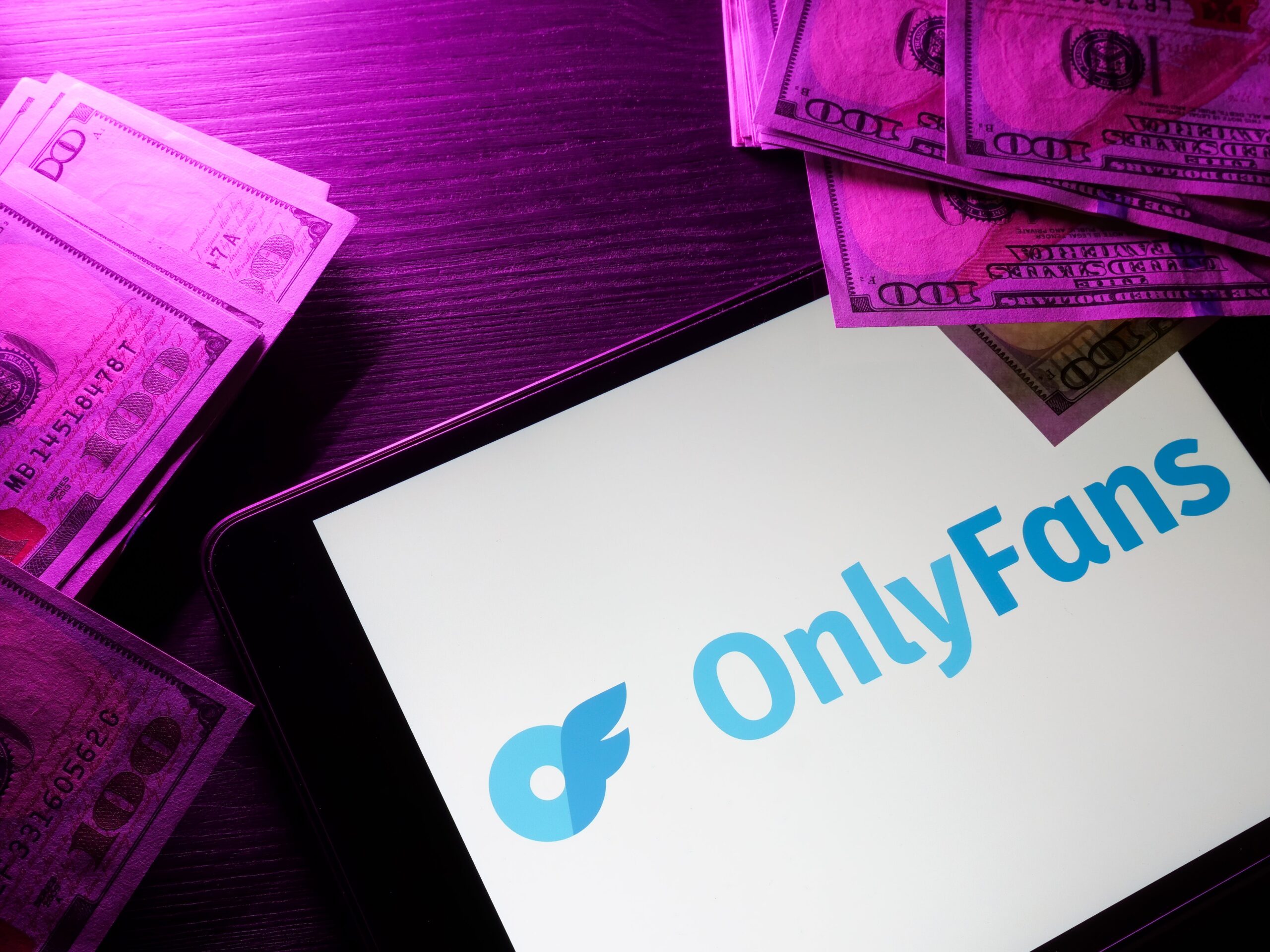 Smartphone screen displaying the OnlyFans logo resting on a desk with purple neon lighting